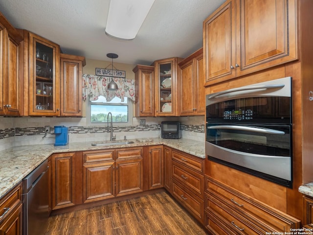 kitchen with light stone countertops, stainless steel appliances, sink, pendant lighting, and dark hardwood / wood-style floors