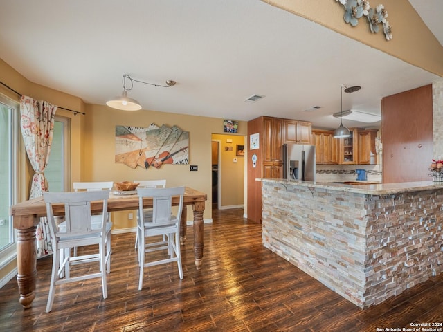 kitchen with kitchen peninsula, stainless steel refrigerator with ice dispenser, tasteful backsplash, dark wood-type flooring, and pendant lighting