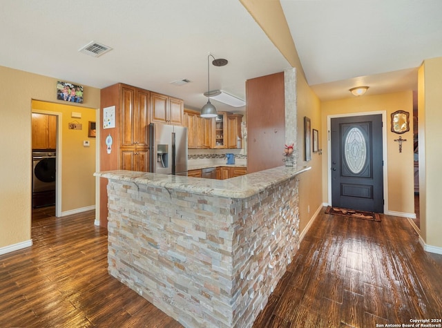 kitchen featuring dark wood-type flooring, stainless steel fridge, light stone counters, kitchen peninsula, and washer / clothes dryer