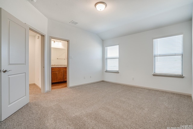 unfurnished bedroom with ensuite bathroom, vaulted ceiling, multiple windows, and light colored carpet