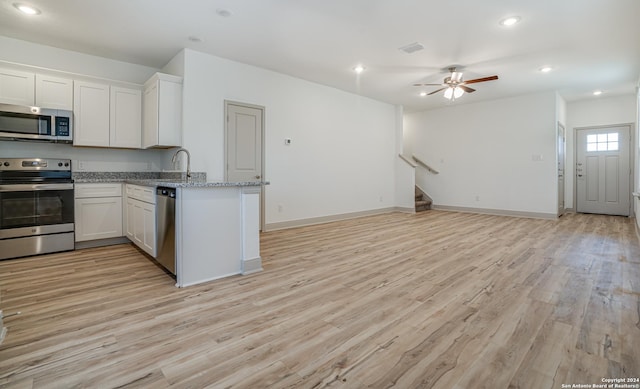 kitchen with light stone countertops, white cabinetry, stainless steel appliances, and light hardwood / wood-style flooring