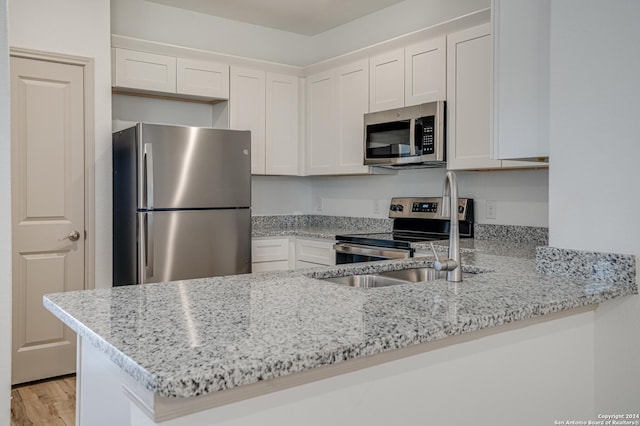 kitchen with white cabinets, kitchen peninsula, appliances with stainless steel finishes, and light hardwood / wood-style flooring