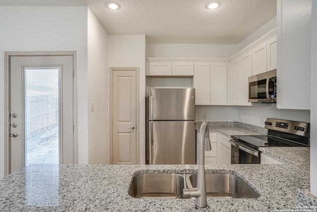 kitchen featuring white cabinets, sink, light stone countertops, a textured ceiling, and appliances with stainless steel finishes