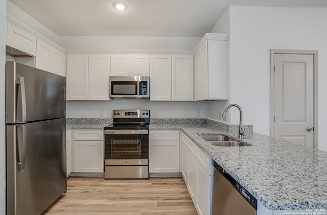 kitchen featuring light stone countertops, white cabinetry, sink, appliances with stainless steel finishes, and light wood-type flooring