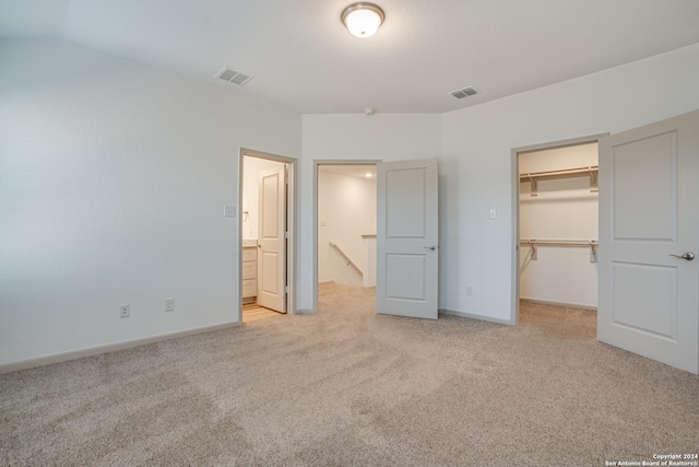 unfurnished bedroom featuring ensuite bathroom, light colored carpet, a walk in closet, and a closet