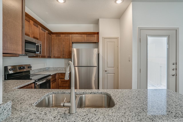 kitchen with light stone countertops, appliances with stainless steel finishes, a textured ceiling, and sink