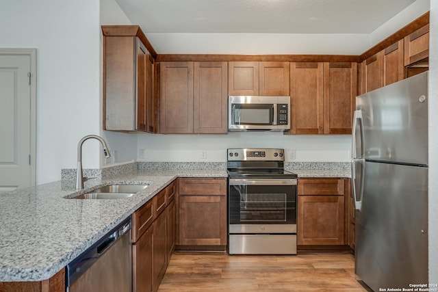 kitchen featuring sink, stainless steel appliances, light stone counters, kitchen peninsula, and light hardwood / wood-style floors