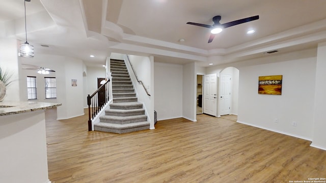 interior space with a tray ceiling, ceiling fan, and light wood-type flooring