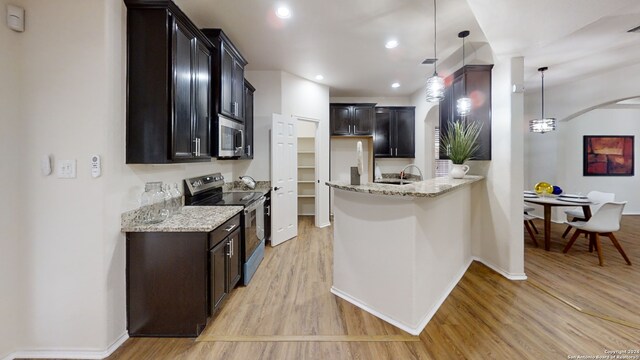 kitchen with light stone countertops, light wood-type flooring, stainless steel appliances, sink, and decorative light fixtures