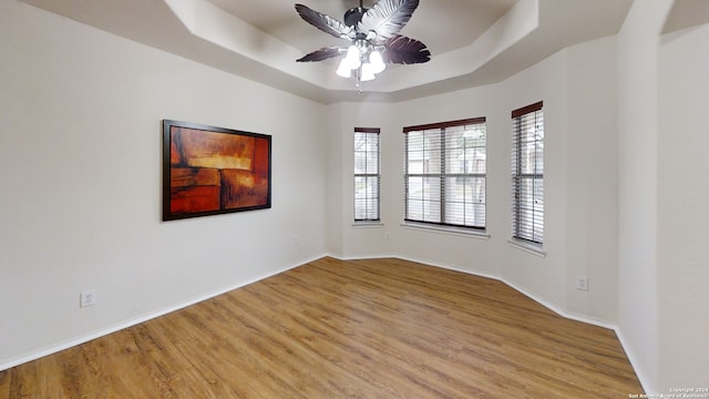 spare room with ceiling fan, light hardwood / wood-style floors, and a raised ceiling