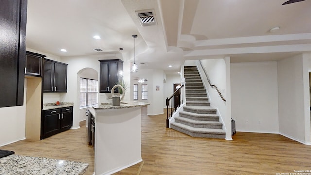 kitchen with light stone countertops, light hardwood / wood-style floors, hanging light fixtures, and a kitchen island with sink