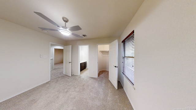 unfurnished bedroom with ceiling fan, a spacious closet, light carpet, and a closet