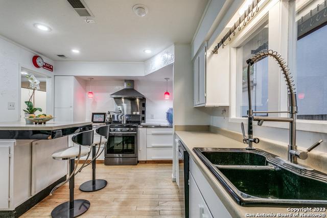 kitchen featuring appliances with stainless steel finishes, light hardwood / wood-style floors, white cabinetry, and wall chimney exhaust hood