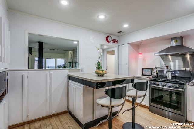 kitchen featuring light wood-type flooring, stainless steel gas stove, white cabinetry, and wall chimney exhaust hood