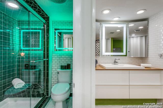 bathroom featuring vanity, a shower with door, backsplash, toilet, and tile walls