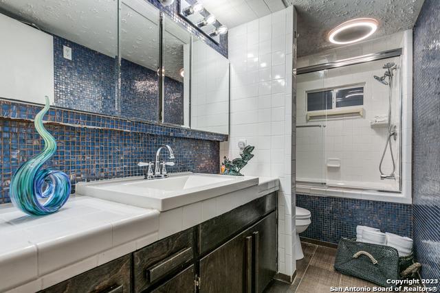 bathroom with vanity, toilet, a shower with shower door, and tile walls