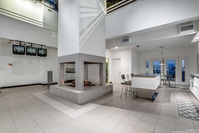 interior space featuring a breakfast bar, white cabinetry, a towering ceiling, decorative light fixtures, and a fireplace