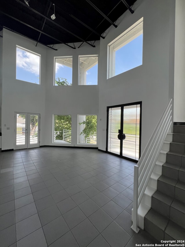 unfurnished living room with french doors, a towering ceiling, and tile patterned flooring