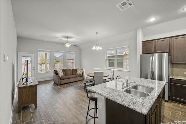 kitchen with a center island with sink, sink, hanging light fixtures, dark hardwood / wood-style floors, and stainless steel fridge