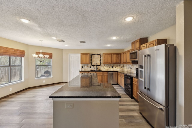 kitchen with a textured ceiling, pendant lighting, stainless steel appliances, light hardwood / wood-style floors, and backsplash