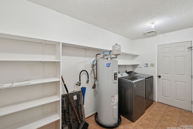 washroom featuring washing machine and dryer, electric water heater, and a textured ceiling