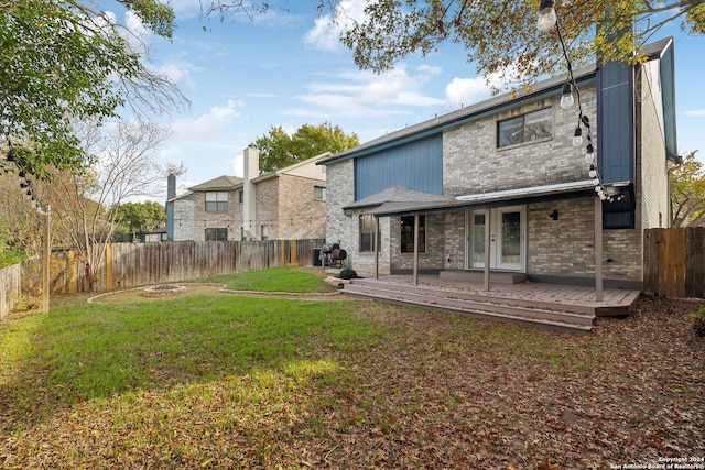 back of property featuring a wooden deck, a fire pit, and a lawn