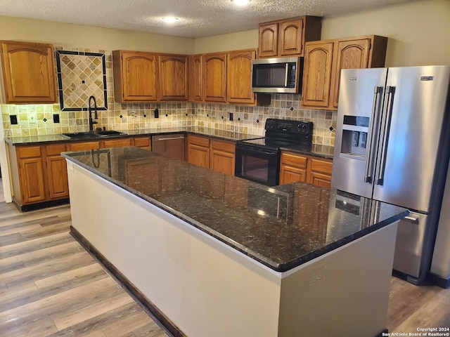 kitchen featuring sink, decorative backsplash, stainless steel appliances, a textured ceiling, and light hardwood / wood-style flooring