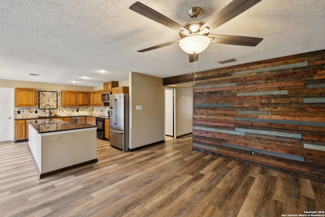 kitchen featuring sink, appliances with stainless steel finishes, wooden walls, a center island, and decorative backsplash