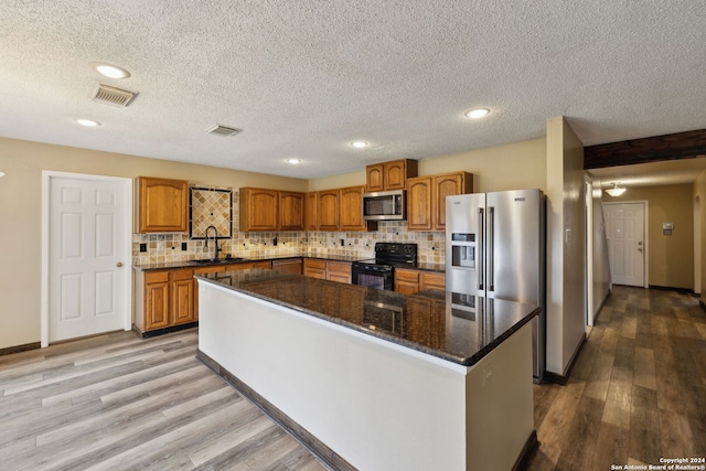 kitchen featuring sink, dark stone countertops, appliances with stainless steel finishes, a kitchen island, and backsplash