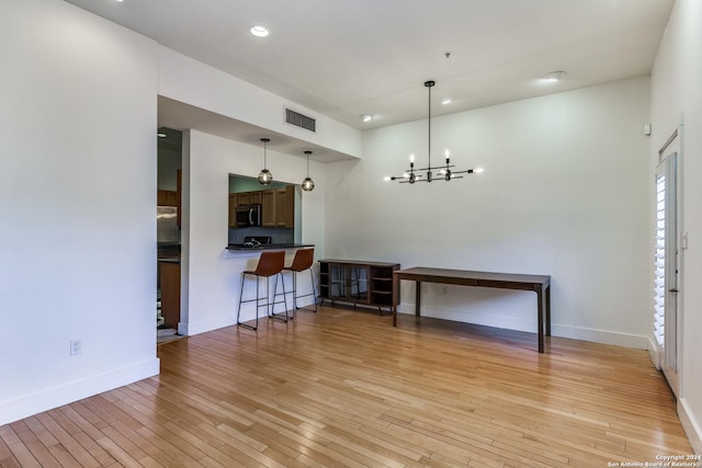 interior space with a notable chandelier, kitchen peninsula, light hardwood / wood-style floors, decorative light fixtures, and a breakfast bar