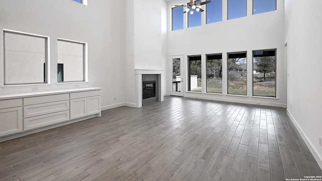 unfurnished living room featuring baseboards, wood finished floors, and a glass covered fireplace