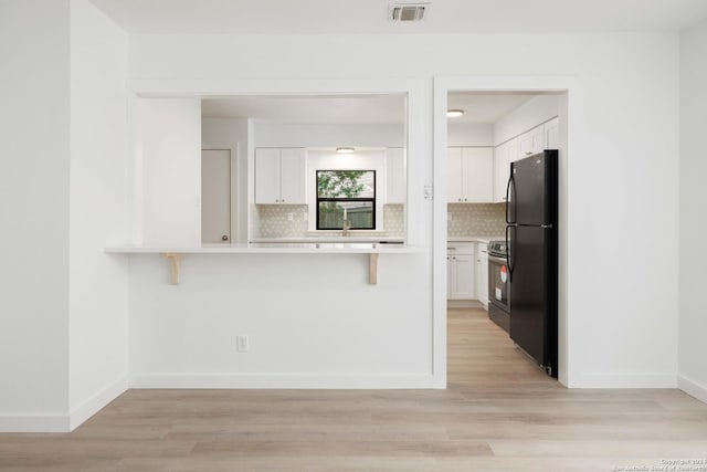 kitchen featuring light hardwood / wood-style floors, decorative backsplash, black refrigerator, and white cabinetry