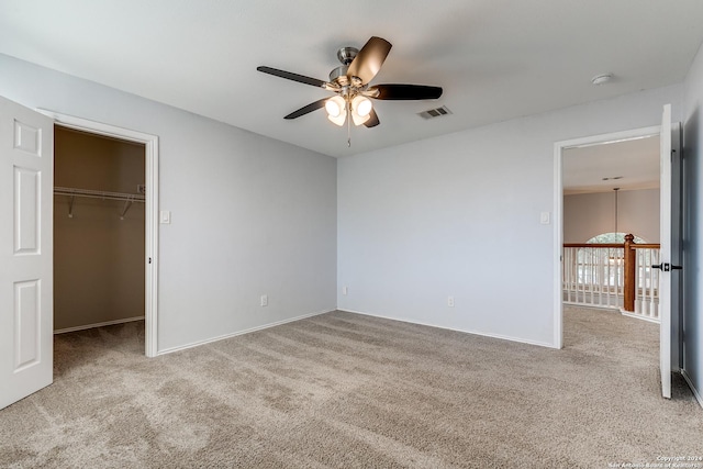 unfurnished bedroom with a closet, light colored carpet, a spacious closet, and ceiling fan