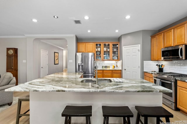 kitchen featuring backsplash, a large island with sink, sink, appliances with stainless steel finishes, and light hardwood / wood-style floors