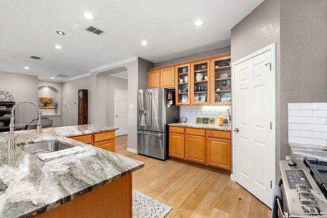 kitchen with sink, tasteful backsplash, light stone counters, high quality fridge, and light wood-type flooring