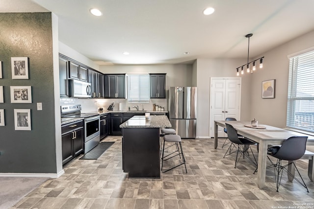 kitchen with light stone countertops, appliances with stainless steel finishes, sink, pendant lighting, and a center island