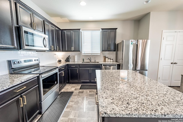 kitchen with a center island, sink, tasteful backsplash, light stone counters, and stainless steel appliances