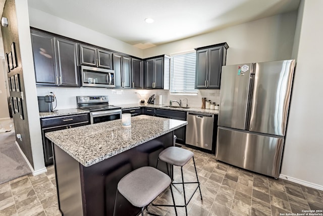 kitchen with light stone counters, a breakfast bar, stainless steel appliances, sink, and a center island