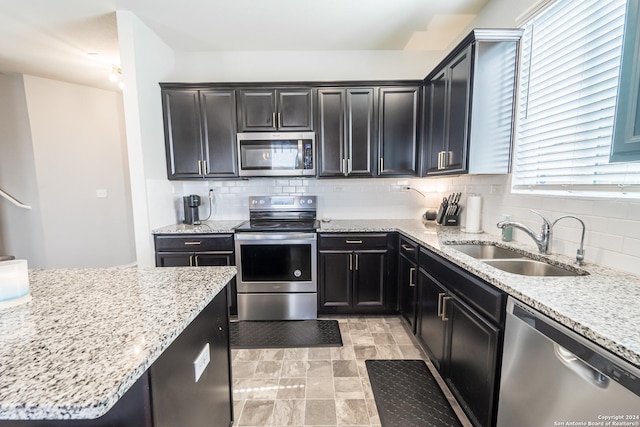 kitchen with appliances with stainless steel finishes, backsplash, light stone counters, and sink