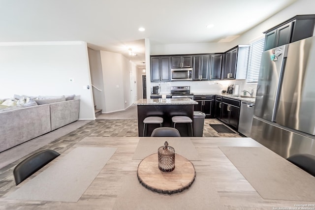 kitchen with a center island, a kitchen breakfast bar, sink, light stone countertops, and appliances with stainless steel finishes