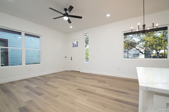 unfurnished living room featuring ceiling fan with notable chandelier and light hardwood / wood-style flooring