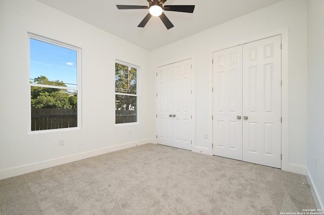 unfurnished bedroom with light carpet, ceiling fan, and multiple closets