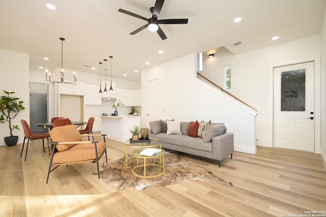 living room featuring ceiling fan with notable chandelier and light wood-type flooring