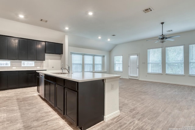 kitchen with lofted ceiling, backsplash, a center island with sink, sink, and light hardwood / wood-style floors