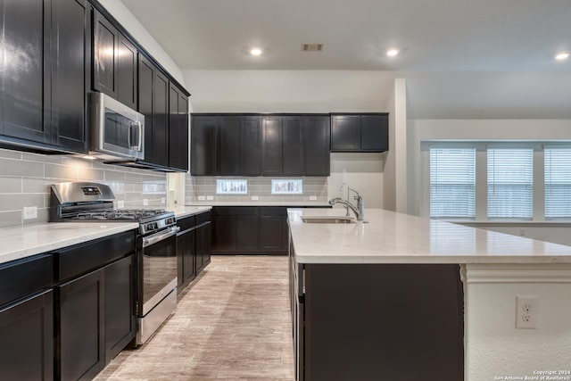 kitchen featuring backsplash, stainless steel appliances, a kitchen island with sink, sink, and light hardwood / wood-style flooring