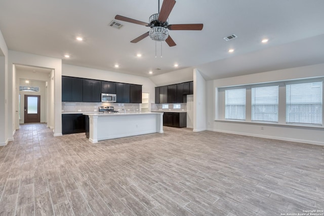 kitchen with tasteful backsplash, stainless steel appliances, ceiling fan, a kitchen island with sink, and light hardwood / wood-style floors