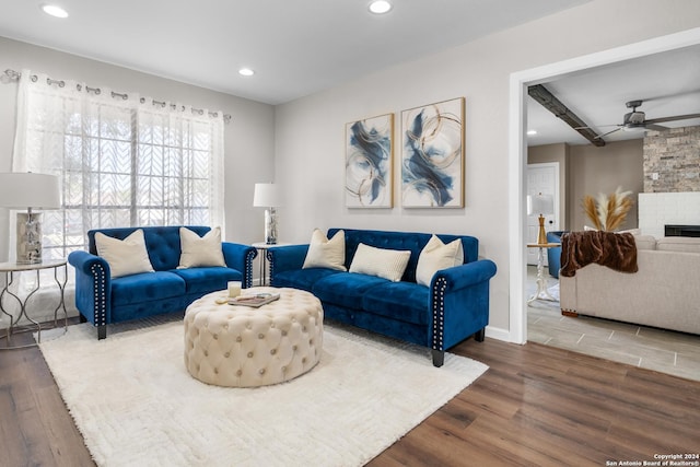 living room featuring hardwood / wood-style floors, ceiling fan, and a stone fireplace