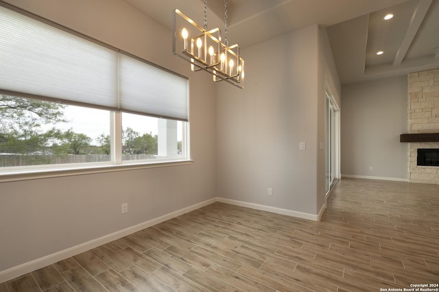 unfurnished room with a stone fireplace, hardwood / wood-style floors, and a chandelier