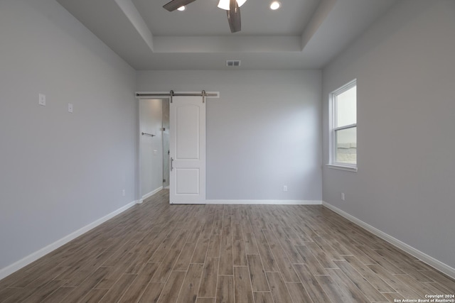 unfurnished room featuring ceiling fan, a barn door, light hardwood / wood-style floors, and a tray ceiling