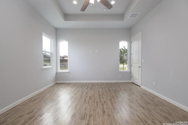 unfurnished room featuring a raised ceiling, ceiling fan, and light hardwood / wood-style floors